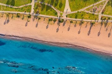 Long shadows of palm trees stretching across sandy beach in early morning sunlight, next to...
