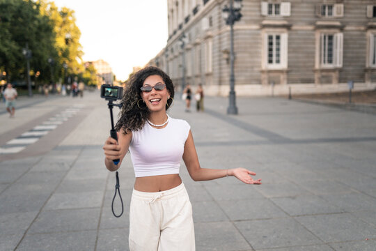 Influencer creating content with an action camera near a European monument during sunset, wearing sunglasses and happily talking to the camera