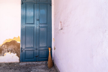A broom rests against a textured wall beside a vintage blue door, showcasing a simple, rustic space filled with character.