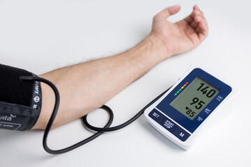 Hands with a tonometer on the table. Man in a shirt measures blood pressure with an electronic tonometer