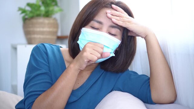 Asian Woman Coughing at Home While Wearing Face Mask , Feeling Sick from Flu, Cold, COVID-19, or PM2.5 Air Pollution Allergies, Showing Health Risks from Virus and Dirty Air