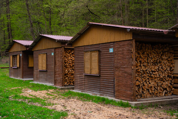 Row of rustic wooden cabins with closed shutters and large stacks of chopped firewood in forest...