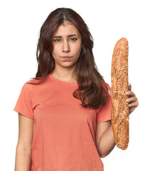 Middle Eastern woman holding bread loaf shrugs shoulders and open eyes confused.