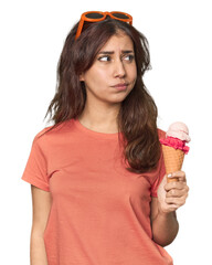 Middle Eastern woman eating ice cream confused, feels doubtful and unsure.