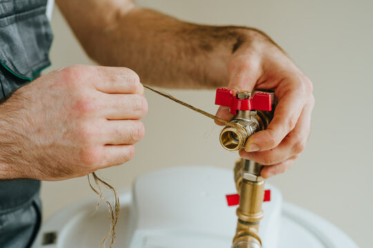 Worker's hands wrapping hemp sealing thread around a metal fitting