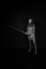 Naklejka premium Slender woman in chainmail and helmet standing and holding sword full length black and white low key portrait