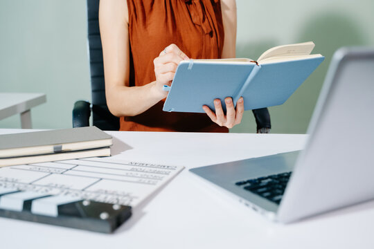 Creative female filmmaker working with tablet, clapperboard, and laptop in modern studio office. Film production, planning, and content creation scene.