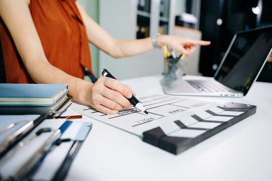 Creative female filmmaker working with tablet, clapperboard, and laptop in modern studio office. Film production, planning, and content creation scene.