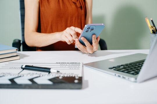 Creative woman multitasking with phone, clapperboard, and laptop while planning film production in a modern studio workspace. Behind the scenes workflow concept.