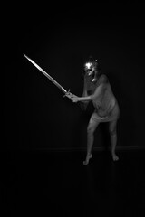 Naklejka premium Slender woman in chainmail and helmet standing and holding sword full length black and white low key portrait