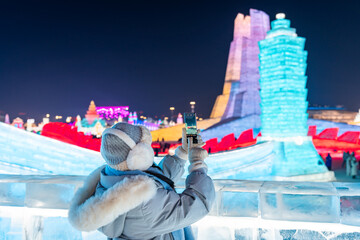 Young happy female tourist enjoying and taking photo in ice and snow world festival at night in Harbin, China