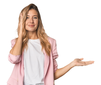 Young blonde in stylish pink suit holds copy space on a palm, keep hand over cheek. Amazed and delighted. - Powered by Adobe