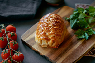 Deliciously Baked Pastry on a Wooden Cutting Board Surrounded by Fresh Vegetables and Herbs