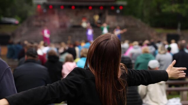 Two people with raised arms enjoy a vibrant live music performance at an outdoor forest stage, surrounded by a cheering crowd in a lively concert atmosphere