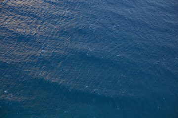 Abstract aerial view of deep blue ocean water surface with subtle ripples and sunlight reflections,...