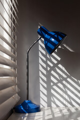 Blue lamp next to bedroom blinds.