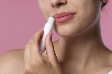 Young woman with lip balm on pink background, closeup