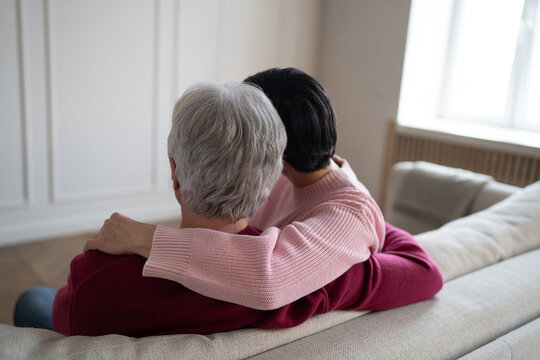 Rearview of loving senior couple sitting on couch embracing hug. Husband stroking wife, peacefully relaxing together at home. Hygge romantic family, warmth comfort, emotional affectionate relationship
