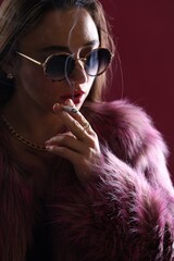 Beautiful woman in fur coat smoking cigarette on dark pink background, closeup