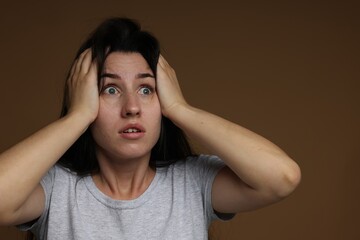 Worried woman suffering from panic attack on brown background