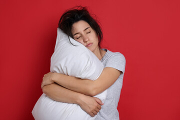 Woman with pillow suffering from hangover on red background