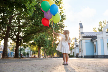 Little girl in dress with bunch of colorful balloons outdoors at sunset, back view