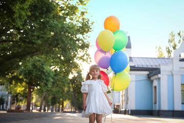 Cute little girl in dress and bunch of colorful balloons outdoors