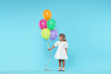 Cute little girl in dress with bunch of colorful balloons on light blue background