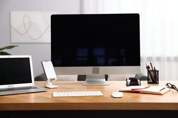 Stylish workplace with modern computer, other devices and stationery on wooden desk indoors