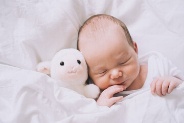 Newborn sleep at first days of life. Portrait of new born baby one week old with cute soft toy in crib in cloth background.