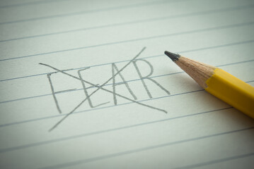 Close up pencil handwriting strikethrough FEAR word on notepad background. No fear or fearless,...