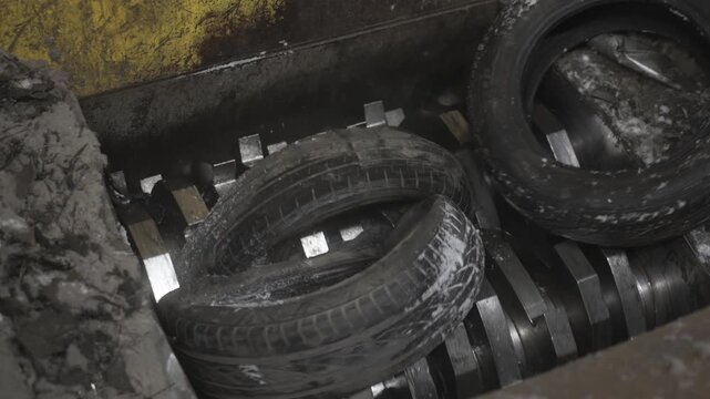 Rubber tires rapidly vanish into continuously spinning shredder teeth. Swift violent relentless mechanical destruction in motion closeup
