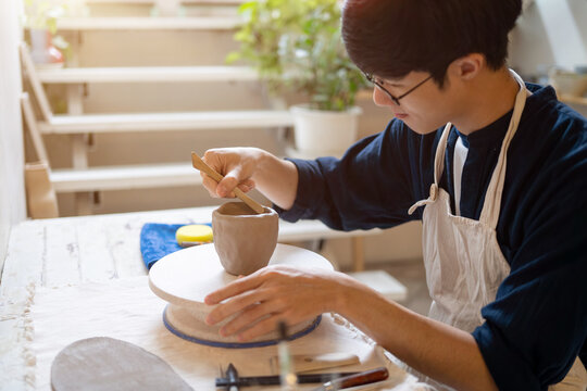 Potter artist holding throwing tool making clay mug cup on working table in pottery class or studio