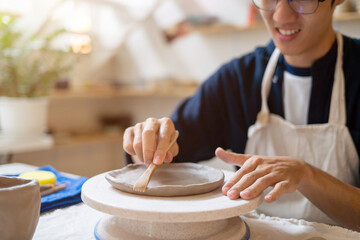Potter artist glasses man molding clay to make a plate on working table in a pottery class or...