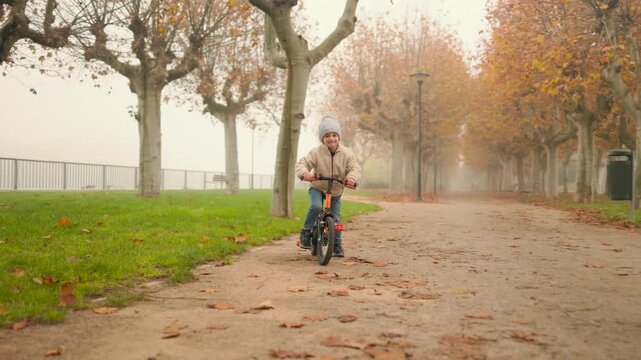 Young child riding balance bike in autumn park.