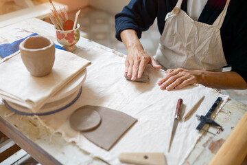 Young man potter artist molding clay to make mug cup on working table in a pottery class or studio.