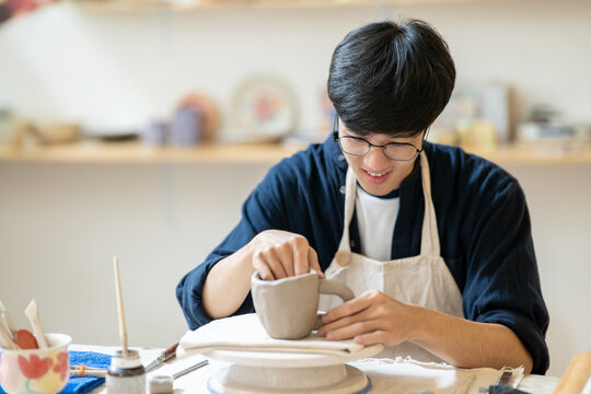 Young man pottery artist molding clay mug cup on throwing wheel at working table in class or studio
