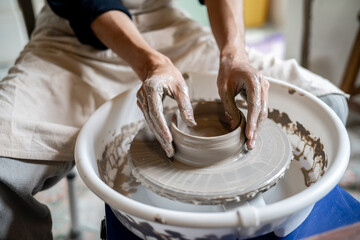 Close up pottery artist hands shaping clay into bowl on spinning throwing wheel in a class or studio