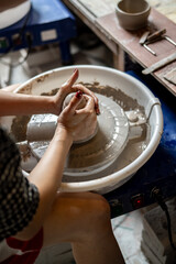 Woman pottery artist with painted nails shaping a clay on spinning throwing wheel in class or...