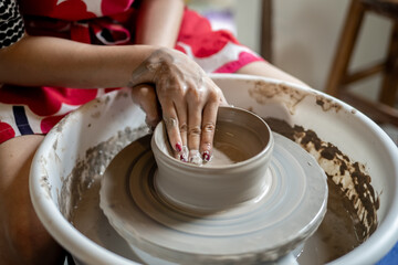Painted nails pottery artist molding clay into a bowl on spinning throwing wheel in class or studio.