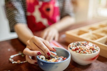 Painted nails woman artist threading ceramic beads making a bracelet or necklace in class or studio.