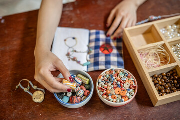 Painted nail pottery artist threading ceramic beads making bracelet or necklace in a class or studio