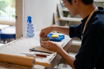 Glasses young man pottery artist molding clay into a mug or cup on working table in class or studio.