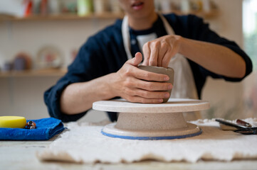 Young man pottery artist shaping a clay mug on throwing wheel at working table in class or studio.