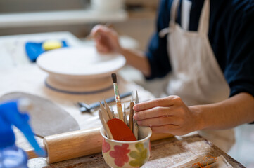 Pottery artist's hand taking a painting brush from ceramic cup on working table in class or studio.