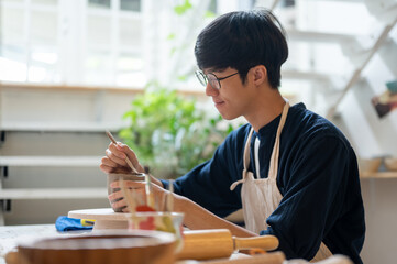 Glasses pottery artist using a throwing tool to make clay mug at working table in a class or studio