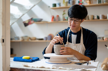 Glasses pottery artist using a throwing tool on clay mug cup at working table in a class or studio