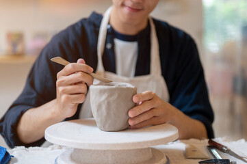 Close up pottery artist using a throwing tool on clay mug cup at working table in a class or studio