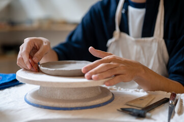 Pottery artist using a scraper to smooth a clay on throwing wheel at working table in class or studio.
