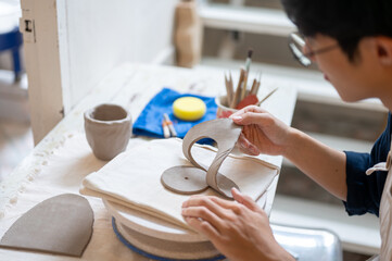 Pottery artist remove circle cut clay off a slab on throwing wheel at working table in class or...